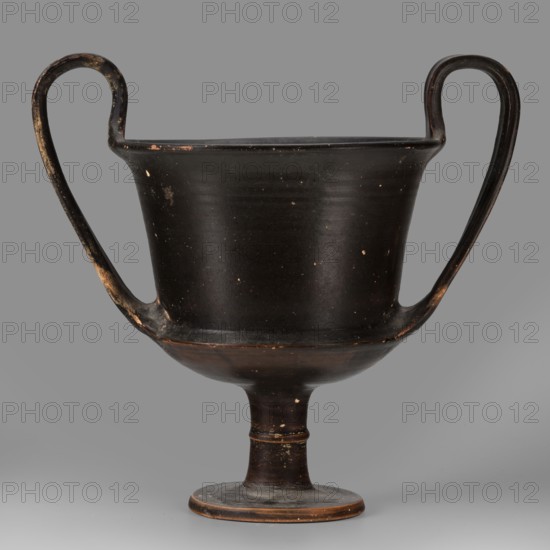 Kantharos, unknown Boeotian workshop. Physical description: Thin-walled kantharos with straight, slightly flared rim edges, a deep cylindrical bowl with an outer edge. The bowl is set on a high leg with a torus in the middle, flat foot. Band-like, wide handles with slightly raised edges, protruding above the level of the rim. The outer surface of the foot is slightly concave. Decoration: Vessel entirely covered with black varnish. Technology: Matte varnish, good quality, evenly distributed. Traces of turning visible under the varnish. Notes: Numerous secondary losses visible on the surface. Attributed to Kamila Nocon; 2nd half of the 5th century BC, Boeotia. Type: kantharos. Weight: 0.552 kg., A dark vessel with a footed base and a wide bowl rising to a flared rim, featuring a pair of high curved handles that extend from the rim down to the lower bowl; the surface shows small worn spots and areas of lighter wear. The predominant color is a deep blackish-brown with patches of lighter br...