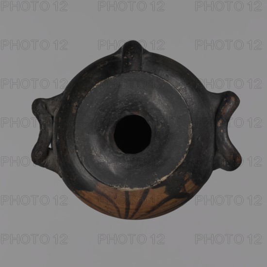 Miniature hydria, antique vessel, hydria vessel, Southern Italy, miniature vessel, Ancient Greece, antiquity; black-figure pottery, red-figure pottery, Greek pottery; reddish clay, black firnis with a matte sheen. Miniature hydria with a disc-shaped foot with a profiled edge, an oval body with slightly rounded shoulders, a high neck, and cylindrical handles. The body is decorated with an 11-petal palmette. 2nd half of the 4th century BC. Hydria; height 11.8 cm, width 7.3 cm., A top-down view of a round ceramic vessel with a central circular opening, showing a mostly dark surface with patches of brown on the lower curved area and some worn lighter spots; the vessel has a pair of small looped handles on opposite sides and a short raised ridge at the top, with visible texture and slight irregularities in the material; colors visible include black, dark brown, light brown, and small areas of pale wear against a neutral gray background.