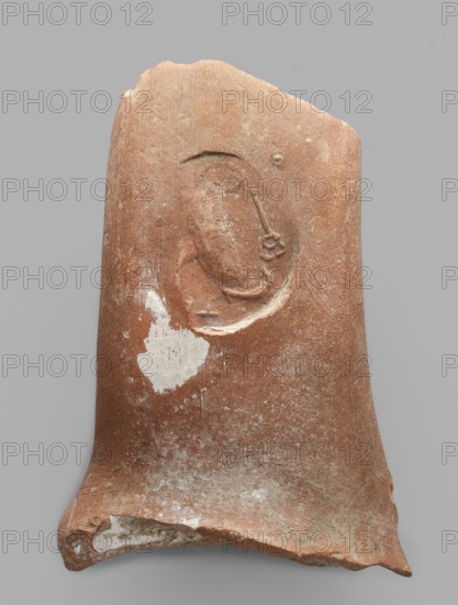 Fragment of an amphora vice behind a stamp, ca. 390 BC, Pantikapaion, Thasos, stamp, vice, height 6.2 cm, width 8 cm, A broken terracotta fragment with a rough, weathered surface showing shades of reddish-brown and patches of lighter beige and white; the fragment has a curved, uneven rim and a recessed oval impression with raised linear and circular details inside it; there is a larger irregular pale patch on one side and scattered lighter speckling across the surface against a neutral gray background.