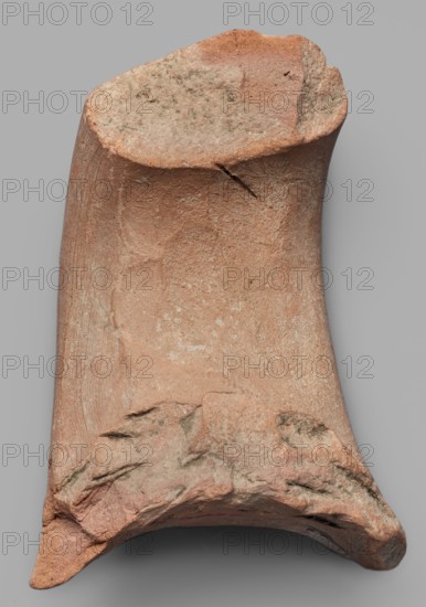 Fragment of an amphora vice, ca. 390 BC, Pantikapaion; Thasos; stamp; vice; height 6.2 cm, width 8 cm, A broken fragment of a hard, rough object with an irregular top and bottom edge, showing a curved, hollowed interior surface and a textured exterior with weathered chips and small cracks; the surface displays a range of colors including reddish-brown, pale pink, light tan, gray-green patches, and darker brown spots, with areas of smoother wear and areas of rough, granular texture.