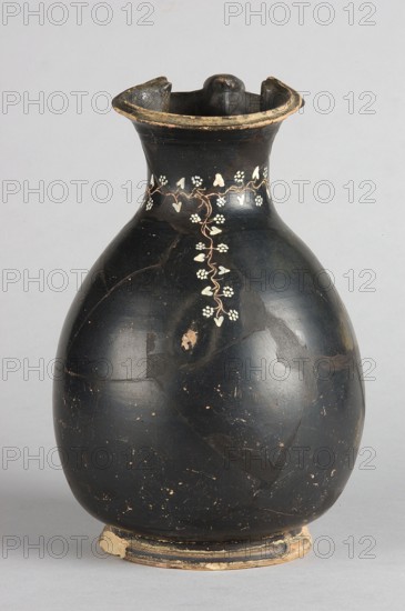 Oinochoe, Gnathia style; decoration: on the neck an engraved horizontal ivy sprig with white-painted heart-shaped leaves and flowers in the shape of pointed rosettes, and a second one extending downwards from it, placed centrally at the front; 2nd half of the 4th century BC, Apulia; oinochoe vessel; height 19.5 cm, width 13 cm., A rounded ceramic vessel with a narrow neck and flared rim, predominantly black in color with areas of worn, exposed lighter clay; a delicate vertical vine-like decoration in a pale color runs down from the neck with small heart-shaped and cluster-shaped leaf motifs; the rim shows chipped edges with a beige exposed layer and the base has a worn bead-like foot with patches of beige and darker paint; the surface of the vessel has a slightly glossy finish with scattered small chips and scratches revealing lighter tones beneath, and the background is a neutral light gray.