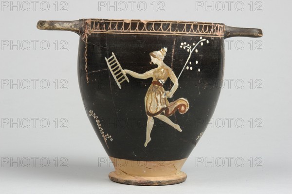 Skyphos, Skyphos with painted decoration. Engraved ornament at the upper edge of the vessel: an egg-shaped structure and a wavy line, framed by parallel lines. At the handles and in the center, vertical, engraved branches with preserved traces of white leaves hang downwards. Side A: a woman shown in left profile with a xylophone in her right hand and a branch in her left. The figure is flanked by small trees on either side. 4th century BC, Apulia, Southern Italy. Skyphos vessel, height 12.1 cm, width 11.1 cm., A black ceramic vessel with a rounded body and a narrow tan base, featuring two short horizontal handles at the rim; painted on the body is a pale-skinned figure in a short skirt and a darker sash, shown in a dynamic pose with one arm extended holding a ladder-like object and the other arm bent while holding a long slender stem topped with small pale dots, with pale decorative motifs around the figure and a patterned border near the rim in tan and brown tones.