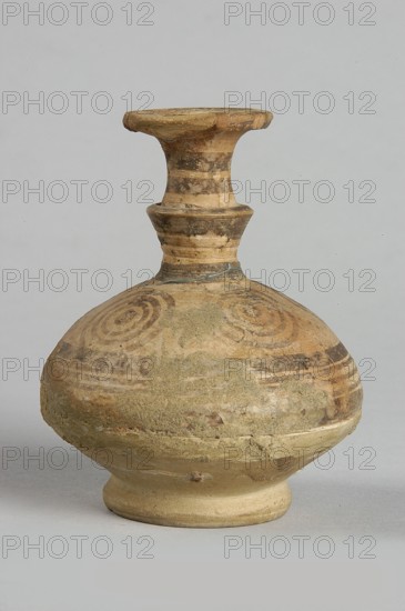 Jug, painted decoration: on the widest part of the body, on the neck and handle - horizontal lines of various widths; on the shoulders - four groups of four concentric circles; on the spout - concentric lines and small semicircles; 850–750 BC, Cypriot Geometric Period III, Cyprus; vessel; height 7.5 cm, width 6.8 cm, A rounded ceramic vessel with a narrow neck and flared rim sits against a pale gray background; the vessel shows worn painted spiral and banded motifs and areas of rough textured surface, with visible chips and patches of residue. The colors visible include beige, tan, light brown, darker brown, and gray.