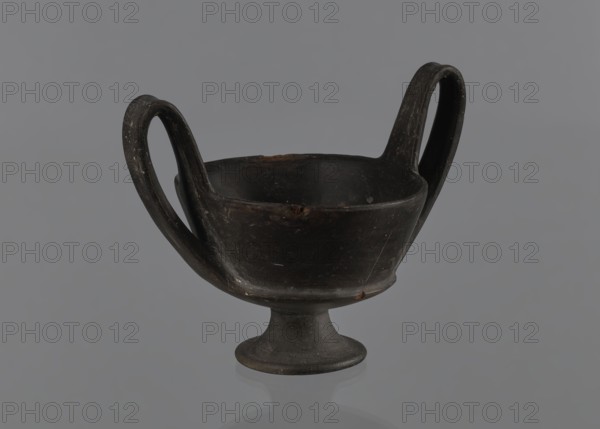 Kantharos, repossession Bytom, vessels, goblets, banquets, Italy, antiquity, Kantharos black-varnished on a cup-shaped foot, 1st half of the 6th century BC, Etruria, vessel, A dark, two-handled cup or bowl with a short pedestal base sits centered against a smooth gray background; the vessel is primarily black with areas of dark brown wear and small lighter scratches, and the handles curve upward and outward creating symmetrical loops on each side.