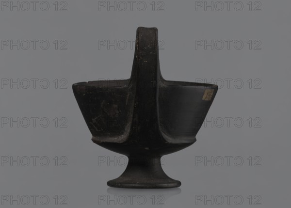 Kantharos, Kantharos black-varnished on a cup-shaped foot, vessel goblet used for banquets, 1st half of the 6th century BC, Etruria Italy, repossession Bytom, antiquity, A dark, matte vessel with a central vertical handle rising from a rounded pedestal base, forming two opposing bowl-like compartments on either side of the handle; the object appears mostly black with subtle brownish wear marks and lighter scuffed areas, set against a uniform gray background.