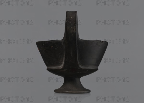 Kantharos, Etruria Italy, repossession Bytom, vessels, goblets, banquets, Italy, antiquity, Kantharos black-varnished on a cup-shaped foot, 1st half of the 6th century BC, Etruria, vessel, A dark, matte object resembling a pedestal bowl with a central vertical handle-like extension is shown against a solid gray background; the object has a rounded base tapering to a narrow stem and flaring into a wide, shallow bowl with two opposing wing-like flares, its surface showing subtle scuffs and uneven patina, and the visible colors are black, dark brown, and gray with small areas of lighter wear.