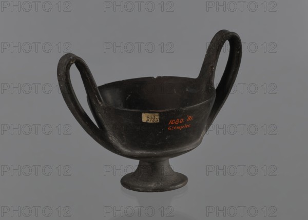 Kantharos, kantharos black-varnished on a cup-shaped foot; vessel used for banquets; goblet form; 1st half of the 6th century BC; Etruria Italy; antiquity;, repossession Bytom., A dark, two-handled vessel with a rounded bowl and a flared pedestal base sits against a neutral gray background; the vessel appears mostly black with subtle variations of dark brown and gray on its surface, and a few small lighter specks and scuffs are visible on the handles and body.