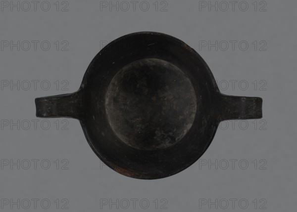 Kantharos, kantharos black-varnished on a cup-shaped foot, vessel; 1st half of the 6th century BC, Etruria Italy; function: goblet for banquets; provenance notes: repossession Bytom., A top-down view of a round, shallow bowl with a broad rim and a pair of short horizontal handles extending opposite each other, all appearing dark and worn with mottled surface textures; the background is a flat neutral gray. The visible colors are black, dark gray, and a few subtle brownish patches.