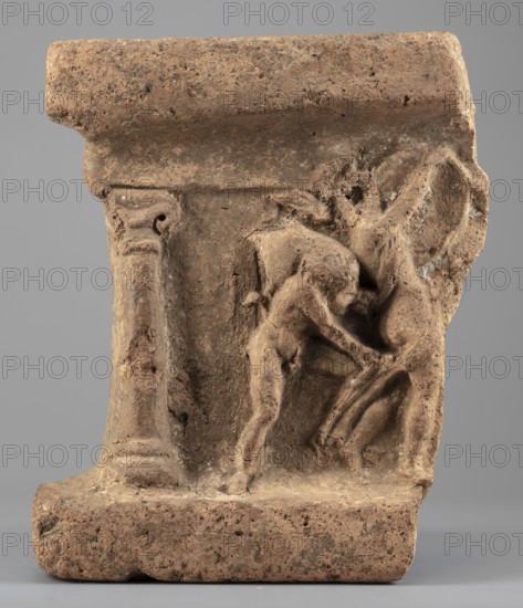 Fragment of an arula home altar depicting a satyr with a wineskin and a maenad with a drum;, Satyr mythology, altars, maenads mythology. Date: 332–30 BC; Hellenistic period previous dating: 3rd–2nd century BC. Origin: Central Italy Italy. Material: altar. Dimensions: height 22.3 cm, width 17.4 cm, depth 7 cm; weight 2.22 kg., A weathered brown stone fragment with a rough textured surface shows a low relief carving of a small nude human figure leaning forward and touching a larger animal-like form; the human form is sculpted with visible limbs and a rounded head, and the larger form has elongated legs and a curved body suggesting movement; the fragment includes architectural elements such as a vertical fluted column section on one side and a horizontal ledge at the top and bottom; the colors visible are shades of brown, tan, and beige with darker brown speckles and occasional lighter whitish patches against a neutral gray background.