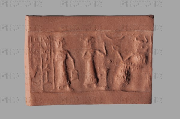 Cylinder seal with a presentation scene and a cuneiform inscription, unknown Akkadian workshop; Mardati scribe. Cylinder with a negatively engraved presentation scene showing three male figures, one seated on a throne damaged and two standing before him. Behind the seated figure are two vertical frames with cuneiform characters. The seated figure is shown in left profile, dressed in a kaunakes-type robe and wearing a headdress with a single pair of horns typical of deities; his right hand is raised in a gesture of greeting toward the approaching figures. In front of him is an altar or censer, and in the upper register is a crescent moon. Behind the altar stands a figure shown in right profile, wearing a long robe finished with fringes; his left arm, bent at the elbow, is raised to face level in greeting, and his right arm, bent at the elbow, is at waist level. Behind the deity, a standing figure in right profile wears a long robe with fringed hem; in his lowered left hand he holds a bu...