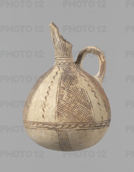 Jug, unknown Cypriot workshop. White painted ware Bronze Age jug with a spherical bottom and a bulging, pear-shaped body transitioning in the upper part into two tubular spouts with protruding walls. A ring-shaped vise protrudes between the spouts. Covered with white paint and decorated with brownish-red paint: a zigzag ornament runs around the body for one-third of its height, flanked on each side by two horizontal lines; below are four bands of lines converging at the bottom. The upper body has four stripes filled with diagonal, intersecting lines, separated by serpentine winding lines. The vise is decorated with diagonal lines at the top and brown paint on the sides. At the base of the rims, a zigzag ornament is framed by two lines on either side; vertical lines surround the rims both inside and outside. Date: 1900–1650 BC. Origin: Cyprus. Vessel; height 15 cm, width 13 cm., An off-white rounded ceramic vessel with a narrow neck and broken spout, featuring a single curved handle; th...