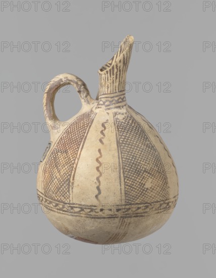 Jug, unknown Cypriot workshop. White painted ware jug with a spherical bottom, a bulging pear-shaped body transitioning in the upper part into two tubular spouts with protruding walls. Between them, a ring-shaped vise protrudes from the body. The vessel is covered with white paint and decorated with brownish-red paint. A zigzag ornament runs around the body for 1/3 of the vessel's height, flanked on each side by two horizontal lines. Below are four bands of lines converging at the bottom. The upper part of the body is decorated with four stripes filled with diagonal, intersecting lines; the stripes are separated by serpentine winding lines. The vise is decorated with diagonal lines at the top and brown paint on the sides. At the base of the rims, a zigzag ornament is framed by two lines on either side; above it, vertical lines surround the rims both inside and outside. Bronze Age, 1900–1650 BC, Cyprus. Vessel; height 15 cm, width 13 cm., An off-white rounded ceramic vessel with a singl...