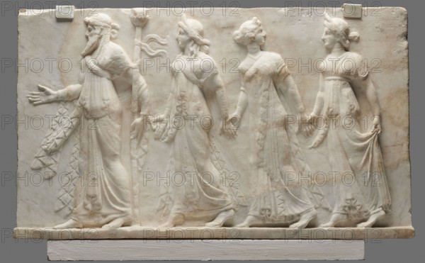 Relief with Dionysus and the Horae, unknown Roman workshop. Rectangular slab cracked in several places with one-sided bas-relief decoration depicting Dionysus with the Horae. Composition is sparse with isocephalism — figures' heads at the same height; despite implied movement, figures appear static. Dionysus wears a long draped Ionic chiton to the ankles, has a long pointed archaic beard, hair with a headband, head in profile, and three locks falling over his left shoulder. His right foot and hand and part of his robe with a zigzag motif are reconstructed. In his bent left arm he holds a thyrsus; his left foot is on tiptoe. The female figures Horae wear archaic chitons decorated with long scarves; the lower garments and feet of the last two figures have been reconstructed. The Horae wear diadems and have hair tied in buns. The central female figure is turned back while the other two, like Dionysus, face forward. Dated 27 BC–14 AD period of Octavian Augustus, 1st century BC probably Q3;...