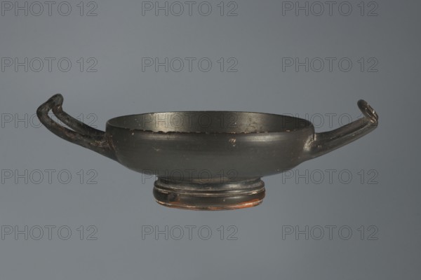 Black-finished goblet, 4th century BC, Campania; vessel goblet; height 5.0 cm, width 12.5 cm., A shallow, round bowl with a low pedestal base and two horizontal handles extending from opposite sides, shown against a plain gray background; the bowl and handles are predominantly dark charcoal to black with worn spots revealing brownish and reddish tones, and the interior and rim share the same dark coloration with small areas of lighter wear.