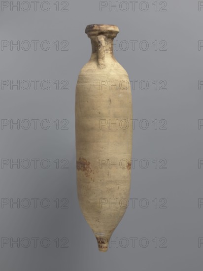 Amphora spatheion, unknown North African workshop Tunisia/Libya. Cylindrical, elongated amphora with a smooth yellow-green surface, probably covered with a coating produced during the firing process natural engobe, self-slip. Two-stage profiled spout with a rounded top and an outward-sloping lip. Small loop-shaped handles attached to the shoulders and to the neck just below the spout; conical bottom. Inner walls covered with a resin impregnation, also visible on the outer walls of the upper part of the amphora. Complete vessel; ceramic body not visible. Date: 2nd half of the 6th–7th century. Provenance: Edfu. Function/type: vessel, amphora spatheion. Dimensions: height 44.2 cm; rim diameter 6.6 cm; body diameter 10 cm., A tall, narrow, elongated pottery vessel with a rounded shoulder, slim neck, and a flared, slightly worn rim, shown against a plain gray background; the vessel surface is predominantly beige with areas of light tan and small patches of darker brown discoloration and spo...