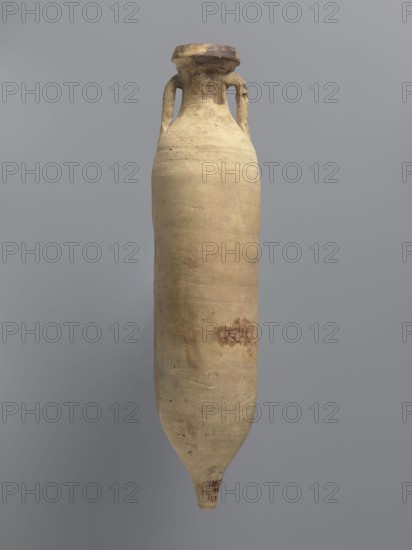 Amphora spatheion, unknown North African workshop Tunisia/Libya. Cylindrical, elongated amphora with a smooth yellow-green surface, probably covered with a coating produced during the firing process natural engobe, self-slip. Two-stage profiled spout with a rounded top and an outward-sloping lip. Small loop-shaped handles attached to the shoulders and to the neck just below the spout; conical bottom. Inner walls covered with a resin impregnation, which is also visible on the outer walls of the upper part of the amphora. Complete vessel; ceramic body not visible. 2nd half of the 6th–7th century. Found at Edfu. Vessel amphora. Height 44.2 cm; rim diameter 6.6 cm; body diameter 10 cm., A tall, elongated ceramic vessel with a narrow, pointed base and a wider rounded body tapering to a short neck with a flared rim, featuring two small loop handles near the neck; the surface appears textured and worn with an overall beige or light tan color, areas of darker brown and reddish-brown discolorat...