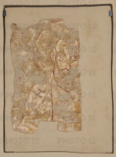 Wall painting: Saint John the Apostle, Nubian workshop; wall painting of John the Evangelist Saint; ?–ca. 100 — iconography. Depicted frontally, preserved fragment showing the head and left shoulder. Head surrounded by a circular yellow halo outlined with purple and white stripe. Facial contours and features painted in black. High forehead, regular eyebrow arches, large almond-shaped eyes wide open with marked irises and pupils, straight nose ending in a wedge, large protruding right ear left ear missing. Long white beard ending in a pointed tip. On the white robe, the Greek letter eta H visible on the figure’s right shoulder. Folds of the robe marked with wide yellow and purple lines. Original plaster. 8th century, Faras. Wall painting. Dimensions: 105 × 78.5 -79 × 4.5 cm; original plaster 82 × 36 cm; height 105 cm, width 78.5–79 cm, depth 4.5 cm, original plaster height 82 cm, width 62 cm., A weathered fragment of painted plaster mounted on a larger pale beige backing, showing an irr...