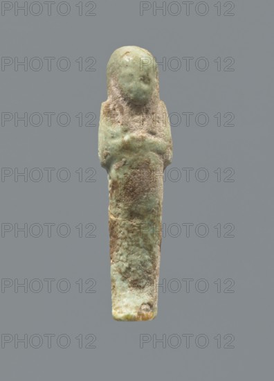 Ushabti, mummy-shaped figurine; funerary gift; hoes. Hands folded on the chest, uncrossed, right hand under left; both hands hold hoes. Smooth tripartite wig with a headband. Facial details poorly legible except for large eyes. Smooth back. No inscription. c. 1069–c. 656 BC, Third Intermediate Period, Egypt. Height 6.4 cm., A small upright figurine with a rounded head and simplified facial area, showing a textured surface with patches of pale green, turquoise, beige, and brown; the body tapers into a narrow rectangular lower portion and the arms are suggested along the sides, with areas of rough, weathered texture and some smoother glazed-looking spots, set against a plain gray background.