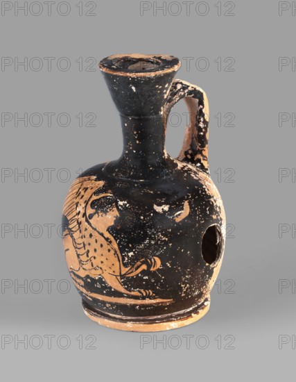 Lekythos with a sphinx, unknown Attic workshop. A small Attic red-figure lekythos. The vessel has a narrow neck, a rounded belly on a circular foot. The central part of the front belly is decorated with an image of a sphinx; the back has worn finials. Ceramic, Greek, 1st half of the 4th century BC, Attica. Height 9.4 cm, diameter 6 cm., An ancient ceramic jug with a rounded body, narrow neck, flared rim, and a single curved handle, showing worn black and terracotta surfaces; the jug's black painted areas are chipped and speckled, revealing terracotta beneath, and a stylized animal motif in terracotta is visible on one side; there is a circular hole on the body opposite the decoration, and the handle and rim display heavy wear with patches of black and terracotta; the overall colors visible are black and terracotta against a neutral gray background.