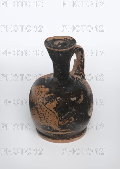 Lekythos with a sphinx, unknown Attic workshop. A small Attic red-figure lekythos with a vase shape. The neck is narrow, the belly round, mounted on a round foot. The central part of the front of the belly is decorated with an image of a sphinx; the back of the vessel has worn finials. 1st half of the 4th century BC, Attica. Ceramic vessel, height 9.4 cm, diameter 6 cm., A rounded ceramic vessel with a narrow neck and flared rim, featuring a single handle extending from the neck to the shoulder; the surface shows worn areas and flaking, revealing the underlying material. The main body displays a painted animal figure with a flowing mane and spotted body, rendered in a contrasting color against the darker background. The rim, handle, and base have chipped edges and patches where the top layer is missing. Visible colors include black, terracotta brown, and lighter beige tones where the surface has worn away.