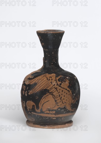 Lekythos with a sphinx, unknown Attic workshop. A small Attic red-figure lekythos with a vise. The neck is narrow; the belly is round, mounted on a round foot. The central part of the front belly is decorated with an image of a sphinx; the back of the vessel has worn finials. 1st half of the 4th century BC, Attica. Vessel; height 9.4 cm, diameter 6 cm., A rounded ceramic vessel with a narrow neck and flared rim, showing a painted figurative scene; the surface is primarily black with exposed areas of natural clay brown where paint has worn or been reserved, and there are scattered lighter tan spots. The body features a stylized animal figure with wings and a tail, rendered in brown against the black ground, with linear hatch marks and dotted patterns on the figure. The neck and rim are mostly black with some brown losses, and the base shows a brown ring along the foot where glaze is missing. Overall the colors visible are black, brown, tan, and lighter beige areas from wear.
