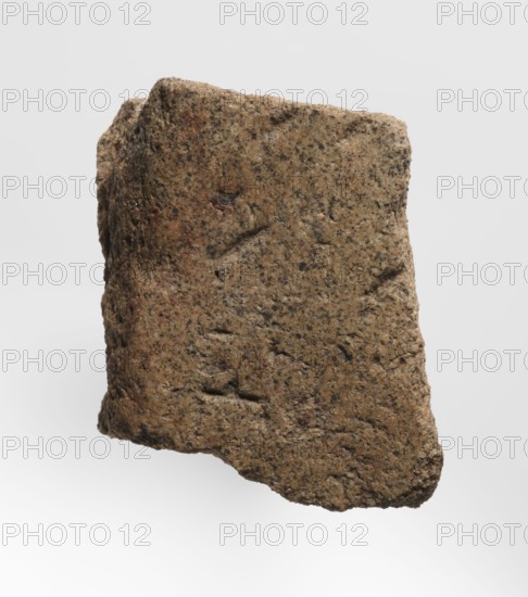 Inscription - fragment, unknown,  craftsman, inscriptions, Granite fragment with engraved hieroglyphic inscription, 760–653 BC; Third Intermediate Period; 25th Dynasty, Old Dongola type of site / place of finding, inscription, height 8 cm, width 7 cm, A roughly rectangular, irregularly shaped rock with a coarse, granular surface in shades of brown, tan, and gray, showing darker speckles and small pits across its face, with rough, uneven edges and a slightly angled top against a pale, light-gray background.