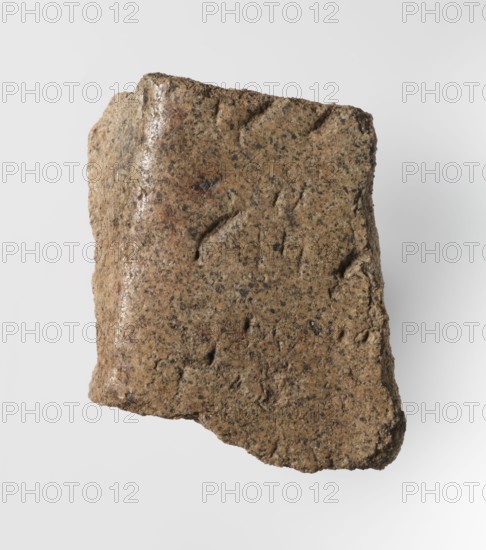 Inscription - fragment, unknown,  craftsman; granite fragment with engraved hieroglyphic inscription; 760–653 BC; Third Intermediate Period; 25th Dynasty; Old Dongola type of site / place of finding; inscription; height 8 cm, width 7 cm, A rough, irregular fragment of stone with a grainy texture and an uneven surface, showing a mix of brown, tan, beige, and darker gray-black speckles; the fragment has worn, chipped edges and shallow shallow depressions and scratches across its face, with one side appearing slightly smoother and glossier than the rest, and the background is a plain light gray.