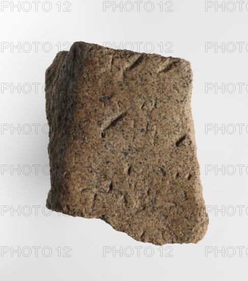 Inscription - fragment, unknown,  craftsman; inscriptions. Granite fragment with engraved hieroglyphic inscription, 760–653 BC; Third Intermediate Period; 25th Dynasty. Old Dongola type of site / place of finding. Inscription. Height 8 cm, width 7 cm., A roughly rectangular piece of coarse textured material with uneven, worn edges and an irregular surface showing small pits and indentations, rendered in shades of brown, tan, beige, gray, and a few darker speckles, photographed against a plain light gray to white background.