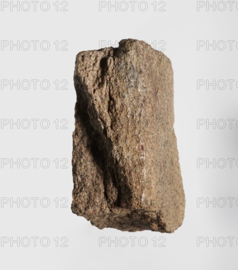 Inscription - fragment, unknown,  craftsman, inscriptions. Granite fragment with engraved hieroglyphic inscription, 760–653 BC; Third Intermediate Period; 25th Dynasty. Old Dongola type of site / place of finding. Inscription, height 8 cm, width 7 cm., A rough, irregular stone with a blocky shape is centered against a pale gray background, showing textured surfaces with jagged edges and a vertical groove; the stone's colors include shades of brown, tan, beige, and hints of darker gray.
