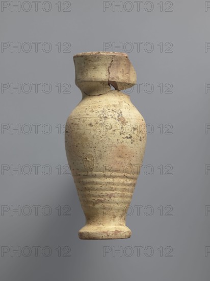 Water vessel qulla. Ovoid with elongated belly; edge of foot protrudes outward. Short, wide neck transitions into a higher, slightly flared section above a sharp break in the wall. Inside the neck a strainer made by puncturing holes in the clay before firing. Entire surface covered with cream-yellow whitewash. Medium-porous Nile clay. 2nd half of the 5th–6th century. Vessel for storing water. Height 17.2 cm; width 9.3 cm; outer rim diameter 7 cm; base diameter 5 cm. Egyptian workshop; Coptic, household vessel., A worn ceramic vessel with a rounded body narrowing toward a small foot and a short neck topped by a broken rim is centered against a plain gray background; the vessel shows a rough, pitted surface with areas of flaking and a mottled palette of beige, tan, light brown, and hints of reddish-brown, and several horizontal incised rings around the lower body.