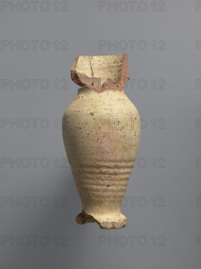 Water vessel qulla. Ovoid, elongated belly; foot edge protrudes outward. Short, wide neck passes into a higher, slightly flared part above a sharp break in the wall. Inside the neck is a strainer formed by puncturing holes in the clay before firing. Entire surface covered with cream-yellow whitewash. Medium-porous Nile clay. 2nd half of the 5th–6th century. Vessel for storing water. Height 17.2 cm; width 9.3 cm; outer rim diameter 7 cm; base diameter 5 cm. Egyptian workshop; Coptic; made at Tell Atrib., A broken clay vessel with a rounded body and a narrow base, showing a rough textured surface in beige and tan with patches of reddish-brown on the rim and base, a missing upper section with jagged edges revealing inner layers, subtle horizontal ridges around the lower body, and a plain gray background.