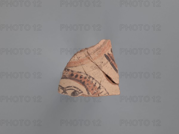 Bottle fragment, unknown North Egyptian workshop; bottles; Egyptian pottery; tableware; figurative and geometric decorations; faces; water vessel qullah; painted Coptic vessel; Coptic pottery; painted Coptic pottery; Nile clay. Fragment of the upper body of a closed vessel, presumably a small-diameter bottle. Red ceramic fabric with a purple core, visible inclusions of gold mica and white-yellow limestone particles. Outer surface covered with white engobe, which took on a cream/cream-pink hue during firing. Interior brown and even. Exterior decorated with black and red paint, part of a larger composition, bordered at the top by a red band with black lines. Below is a fragment of a human head: arched eyebrows and round black pupils looking to the side. Hair indicated by many small dots painted on a red background. To the right of the head is a group of straight vertical black lines on a red ground. 6th–7th century, Tell Atrib; vessel bottle. Height 4.4 cm, width 6 cm., A broken piece of...