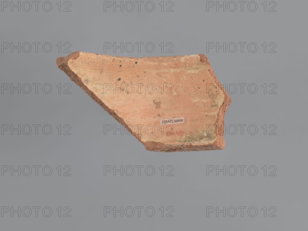 Fragment of a vessel stand, painted Coptic vessel stand with floral decorations. The walls form a hoop with the upper edge diameter slightly larger than the lower. Decoration painted in black and red on a beige whitewash background. The lower edge bulges outward and inward in a half-cylinder form; its outer surface has a black horizontal band. The upper edge has an outward rim whose horizontal outer surface bears a red band with several black dots and a series of lines running perpendicular to the rim. Exterior decorated with almond-shaped, stylized, unevenly sized plant elements with pointed tips, each filled with a grid of black lines and surrounded by two or three groups of arcuate lines repeating its shape. Medium-porous Nile clay. 6th–7th century, Tell Atrib; vessel. Height 8.5 cm, width 13.7 cm, lower outer rim diameter 24 cm, upper outer rim diameter 25 cm., A broken piece of pottery or tile is shown against a plain gray background; the fragment has an overall terracotta and red...