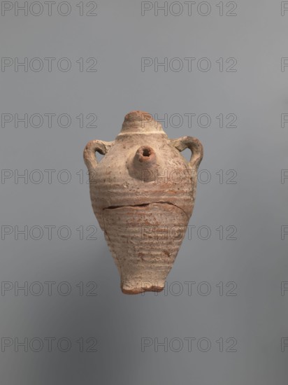 Water vessel qulla. Ovoid, elongated body, wider in the uppermost part above half the vessel's height. Low foot, hollow inside, poorly defined externally. Two small vises are glued to the arms, and between them, on an axis perpendicular to their attachment, a conical spout for drinking water is glued. Neck preserved in its lowest part is separated from the body by a small, sharply profiled hump. Entire surface covered with light whitewash. Nile clay, medium-porous. 5th century. Vessel; height 17.0 cm, width 11.5 cm, base diameter 4 cm., An aged clay vessel with a tapered base and a rounded shoulder floats against a gray background, showing a weathered surface in shades of light brown, beige, and terracotta with rough, horizontal ridges and patches of darker brown; the vessel has two small rounded handles near the top and a short spout protruding from the shoulder, and the rim and spout areas display chipped, uneven edges and subtle texture variations.