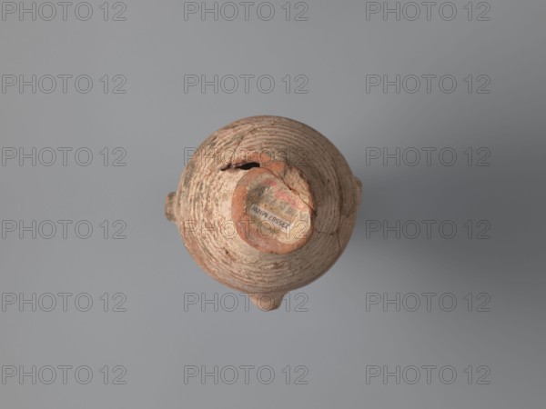 Water vessel qulla, bottles, Coptic vessels, water vessels qullae, qulla, Water vessel bottle, gulla. Ovoid, elongated body, wider in the uppermost part, above half the vessel's height. Low foot, hollow inside, poorly defined externally. Two small vises are glued to the arms, and between them, on an axis perpendicular to their attachment, a conical spout for drinking water is glued. The neck, preserved in its lowest part, is separated from the body by a small, sharply profiled hump. The entire surface of the vessel is covered with light whitewash. Nile clay, medium-porous, 5th century, Tell Atrib, vessel, height 17.0 cm, width 11.5 cm, diameter 4 cm base, A top-down view of an old rounded clay vessel with a narrow neck and a broken rim, showing a textured, weathered surface in shades of brown, tan, and reddish-orange, set against a smooth gray background; a few small areas of darker discoloration and rough patches are visible on the vessel.