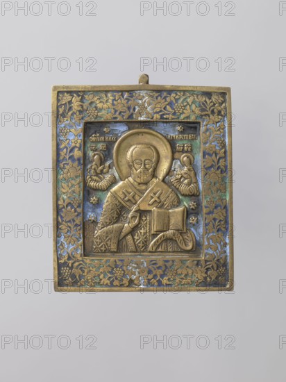 Icon: Saint Nicholas the Wonderworker. Russian workshop. Nicholas of Myra ca. 270–352. In the center, St. Nicholas is shown frontally, half-length, with an open Gospel book in his left hand and giving a blessing with his right; wearing a phelonion and an omophorion around his neck. The saint's face is broad, with a high forehead, a short semicircular beard, and a halo. On either side of Nicholas—reduced in size and clouded to his knees—are Christ offering the saint a book and the Mother of God presenting the omophorion. Stars appear in the background and an identifying inscription is at the top. The whole is surrounded by a wide frame with a plant ornament vines and flowers. The background and frame are covered with blue, navy blue, green, and black enamel. Late 19th century, Russia. Icon. Height 11 cm; width 10 cm; depth 0.4 cm., A rectangular metal icon with a raised central panel showing a bearded haloed figure wearing a patterned robe and holding an open book, flanked by two smalle...