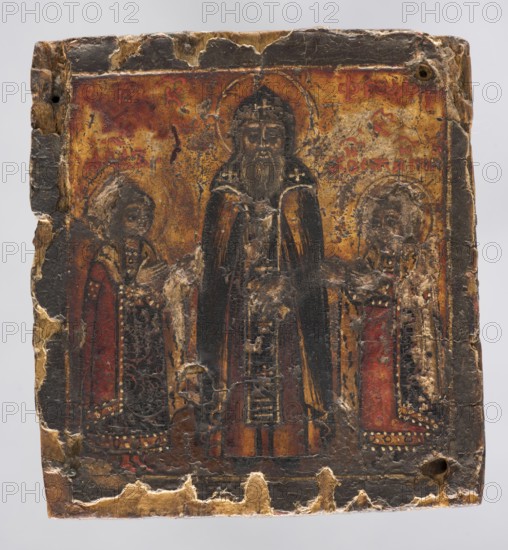 Icon: St. Theodore with His Sons — David and Constantine. Stroganoff School 1550-?. Attributed author unknown. Depicts three standing figures: in the center the holy monk Theodore, Prince of Smolensk; on either side, in reduced size, his sons Princes David and Constantine. Inscriptions present. Icons; saints; princes. 2nd half of the 18th century, Russia. Icon; height 6.5 cm, width 5.9 cm., An aged rectangular panel shows a worn painted scene with three standing robed figures; the central figure is taller with a dark long robe and a halo, flanked by two smaller figures in patterned garments with halos. The background is mottled with warm tones of gold and brown with areas of red, while the robes include dark black, deep red, and muted orange hues, and there are flecks of lighter beige where the surface has peeled. The panel edges are chipped and frayed, revealing raw wood in pale tan and beige, and there are several areas of cracking and loss across the painted surface.