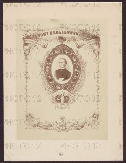 To Jan Królikowski on the 35th anniversary of his artistic profession. 14/4 1873, Kloch, Ferdynand i Dutkiewicz, Melecjusz photographic studio; 1866–1874 authors, Gerson, Wojciech 1831–1901 draughtsman; co-author, Królikowski, Jan Walery 1820–1886, male portraits; iconography of Jan Walery Królikowski; portraits; actors; theatre artist; anniversaries; photographic tableau; theatre costumes; print glued with the entire surface onto cardboard; 1873; Warsaw; photography; photographic tableau; reproduction of a work of art; photographic print: 25.1 × 19.0 cm; cardboard: 32.9 × 24.7 cm, A sepia-toned ornamental print featuring a central oval portrait of a man wearing a dark jacket and white shirt, set within an elaborate decorative frame with floral wreaths and small portrait medallions; above the oval is a curved ornamental banner and scrolling foliage, and below it is an ornate cartouche with decorative figures and flourishes; the composition is bordered by vertical floral garlands on bot...