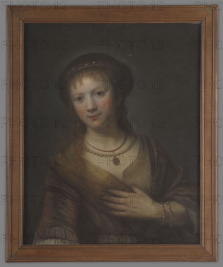 Saskia von Uylenburgh 1612–1642, wife of Rembrandt; copy after Rembrandt van Rijn 1606–1669. Half-length, full face portrait, after 1641. Light hair falling on the shoulders and forehead; wearing a beret decorated with stones, a golden dress with a large neckline and a shawl over her shoulders. Around her neck: a string of pearls and a medallion with a blue stone on a chain. Her left arm, bent at the elbow, is decorated with two golden bracelets that support the coat on the chest. Background dark and plain. This is a fragment from Rembrandt’s painting Saskia with a Red Flower; in this portrait the flower is not visible, only the outstretched arm. Portrait, height 64.5 cm, width 54 cm., A framed portrait of a person shown from the waist up wearing a dark head covering and a layered outfit with a shawl; the background is dark gray to black, the frame is brown wood, the person has light skin with pinkish cheeks, light brown hair, and blue-gray eyes, and they wear a few necklaces and a pen...