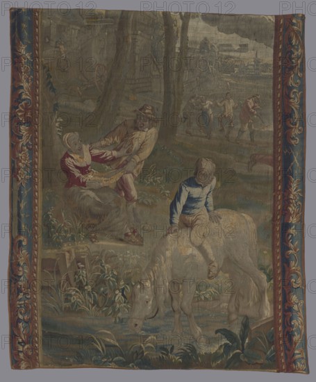 Tapestry, In the foreground a boy on a horse on the river bank; in the background dancing peasants against the background of buildings; 18th century; tapestry; height 190 cm; width 154.5 cm., A woven scene framed by decorative borders in blue, red, gold, and cream shows a pastoral setting with trees and grassy terrain. In the foreground a pale cream-colored horse stands with its head lowered toward water, and a young person wearing blue and tan sits sideways on the horse. To the left a seated figure in red and cream reaches toward a standing figure in tan and brown who appears to wear a hat; foliage and plants in shades of green surround them. In the middle distance a group of people in muted tones move together on a path, and farther back there are indistinct buildings and landscape elements in gray, brown, and green under a cloudy sky. The overall palette includes blues, greens, browns, creams, reds, and golds.