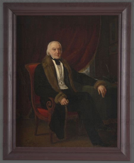 Karol Otto Kniaziewicz 1762–1842, unknown author. Figure sitting on a Hamburg armchair upholstered with red fabric, three-quarters turned to the right. Gray hair, hazel eyes. Dressed in a black coat with collar and cuffs trimmed with brown fur; beneath it black clothing, a white vest and a white shirt with a bustier. A black cravat around the neck. The left hand rests on a table covered with green cloth; next to it are an inkwell, writing implements and a paperweight, above two paintings. In the background a red curtain revealing part of a landscape. Before 1842, Paris. Portrait. Height 55.6 cm, width 42.5 cm., A seated older man with pale skin and white hair wears a dark coat trimmed with brown fur over a light vest and dark bow tie, sitting in a red upholstered chair; a dark red drapery hangs behind him and a dark green surface with objects is visible to his side, with his hands resting on the chair arm and the surface. The overall palette includes shades of dark brown, deep red, dar...