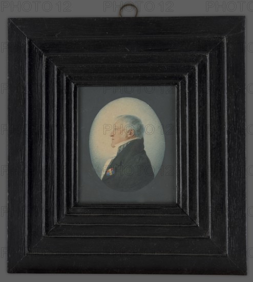 Karol Otto Kniaziewicz 1762–1842, unknown author. Bust of a man in left profile. Blue eye, grey-blond hair. A white shirt with a high collar, a light-striped vest, and a black tailcoat with a red, blue, and gold ribbon pinned to the left lapel. Blue background. Depicted in civilian attire with the berets of the Legion of Honor and the Virtuti Militari Cross, fastened with a gold plaque with diamond stars. Two similar miniatures: one of General Stanislaw Fiszer and one of Lieutenant Colonel Ignacy Hauschild, circa 1810. A copy of the miniature was made in 1815 by Aleksandra Radziwillowa née Stecka, the general's stepdaughter, in the album of Ludwika Antoniowa Radziwill, after 1815, Poland. Type: miniature., A framed oval portrait of an older man in profile, set within a rectangular multi-stepped black wooden frame with visible wood grain and a small metal hanging loop at the top; the man has light gray hair and pale skin, wears a dark coat with a high collar and a white cravat, and a sm...