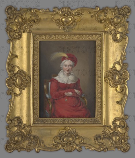 Helena Radziwill, née Przezdziecka 1752–1821, with grey hair, in a red dress, sitting on a chair with her arms folded; on her head a bonnet with an egret. The grey hair and clothing indicate the portrait dates from 1815–1820, when Helena would have been about 63–68 years old; earlier suggestions that she was pregnant in the portrait are considered impossible given the date. Painted by Ernst Gebauer 1782–1865. 1815–1820, Poland. Portrait miniature, 15.5 cm × 11.8 cm., A framed oil portrait of a seated woman wearing a red dress and a matching red head covering with a yellow feather, a white ruffled collar around her neck, pale skin and white curled hair, hands folded in her lap holding a small pendant, seated in a wooden chair with blue upholstery, against a dark neutral background; the portrait is set within an ornate gilded frame with elaborate scrollwork and decorative carved motifs in gold.