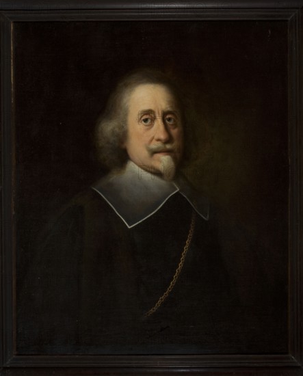 Man with a white Spanish beard; unknown painter; 1640–1660; portrait; height 79.0 cm, width 64.6 cm also listed as 79 × 64.5 cm., A framed oil portrait of an older man shown from the chest up against a dark background, with pale skin and light gray hair that is wavy and shoulder-length; he has a small pale beard and mustache. He wears a dark garment with a broad white collar edged in a thin dark line, and a gold chain draped across his chest. The overall color palette includes dark brown and black tones in the background and clothing, pale beige and pink in the face and beard, white in the collar, and gold in the chain, with the frame appearing dark brown.