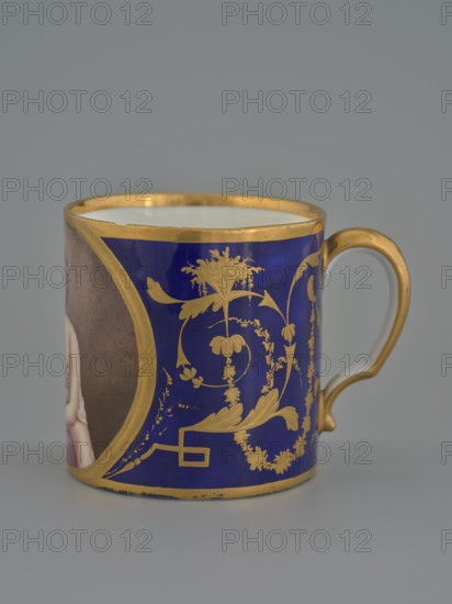 Cup, Manufacture nationale de porcelaine de Sèvres est. 1756, 1803–1804, hard-paste porcelain, vessel, height 7.5 cm, A close-up of a ceramic cup with a curved handle, showing a deep cobalt blue surface decorated with ornate gold-painted floral and scroll motifs and gold trim along the rim and base; the handle is painted gold on the outside and white on the inside, and a small portion of a painted portrait with flesh tones and brown background is visible at the left edge.