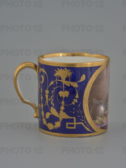 Cup, Manufacture nationale de porcelaine de Sèvres est. 1756 manufacturer, 1803–1804, hard-paste porcelain vessel, height 7.5 cm., A cylindrical ceramic cup with a curved handle sits against a neutral gray background, showing a deep cobalt blue surface decorated with ornate gold painted floral and scroll motifs and gold rims along the top and bottom edges; the handle is gold, and a partial painted oval panel on the side reveals muted brown and pink tones with small floral elements, while the interior of the cup is white.