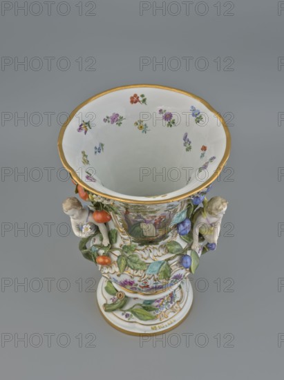 Vase, 19th/20th century, Meissen; vase; diameter 36 cm; base diameter 24 cm; formerly associated with Radziwill palace Nieborów., A porcelain vase photographed from above showing a wide flared rim with a gold edge and a white interior decorated with a few small painted flowers in colors including purple, red, yellow, blue, and green; the exterior features painted scenes and relief decorations with a group of leaves and fruit in green, orange, and blue, and two small sculpted cherub-like figures in pale skin tones positioned on opposite sides; additional decorative elements include gold accents and multicolored floral motifs on a white background, all set against a plain gray backdrop.