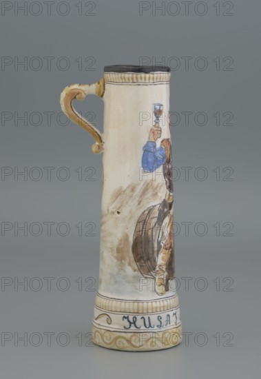 Mug. Cylindrical mug, slightly tapering toward the top, with a handle. Mantle decorated with an image of a nobleman sitting on a barrel holding a glass goblet in his right hand; a coat of arms next to the handle; plant decoration. Inscription on the pedestal: Hulaj dusza. Tankard; height 28 cm, width 15 cm with handle, inlet diameter 6.5 cm, bottom diameter 9 cm. Majolica manufactory in Nieborów manufacturer, 1881–1899. Maker: Jadwiga Hyzycka 1856–1922, 1881–1890., A tall ceramic tankard with a curved handle painted in shades of tan and ochre stands against a gray background; the body of the tankard is primarily off-white with painted figures in blue, brown, tan, and black, including a person raising a cup and parts of a wooden barrel, and decorative bands in yellow ochre and black near the top and base.