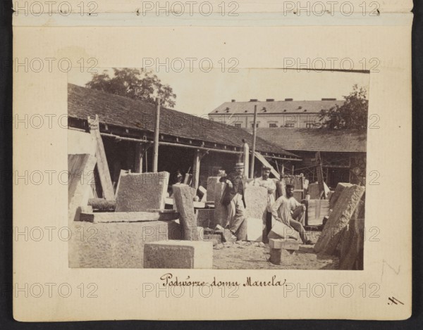 The Courtyard of Mancel's House View of the stonemasonry and sculpture workshop of Jan Józef Manzel. In the center the sculptor Józef Manzel, the owner's son, photograph by Karol Beyer 1818–1877; subjects: Jan Józef Manzel 1806–1875, Józef Manzel 1834–1904; other photographer: Leopold Méyet 1850–1912. Date: 1861–1863. Place: Warsaw Chlodna street. Genre: photography, nature photography; depiction: sculptors, sculptors' workshop, iconography. Photographic print: 5.7 × 8.4 cm; support: 11.3 × 8.8 cm., The image shows a sepia-toned scene of an outdoor yard with a group of several people among many large stone blocks and carved slabs, a few leaning against one another and several scattered on the ground; a long single-story building with a sloped roof runs along the background, with a taller multi-story building partially visible behind it and some trees rising above the roofs; a few vertical poles and wooden supports stand among the stones, and one person sits on a block while others stan...