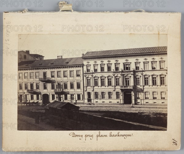 Houses at Bankowy Square Eastern frontage of Rymarska Street with Kruzy and Flatau's tenement houses, photograph by Karol Beyer 1818–1877, showing Kruzy tenement house Rymarska 8 and Flatau's tenement house Rymarska 10, Rymarska Street, Bankowy Square, Warsaw; dated 1861–1863. Photographic print, nature photography; image size 6.2 × 9.5 cm; support 11.3 × 8.8 cm. Additional iconography: Julian Ankiewicz 1820–1903, Alfons Kropiwnicki 1803–1881, photographer Leopold Méyet 1850–1912 noted., A sepia-toned photograph shows a row of connected multi-story buildings with ornate façades and rectangular windows, some featuring decorative window surrounds and small balconies. The buildings have pitched metal roofs and a mix of lighter and darker wall tones, primarily beige, cream, and brown, with darker gray and black roof areas. In front of the buildings is an open area with a low structure or shed with a slanted roof in darker brown and black tones, a stretch of ground or pavement, and a few in...